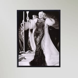 Peut inclure: Photographie en noir et blanc d'une femme portant une longue robe noire transparente à motif floral et un manteau en fourrure blanche. Elle se tient sur une scène avec un microphone à la main.