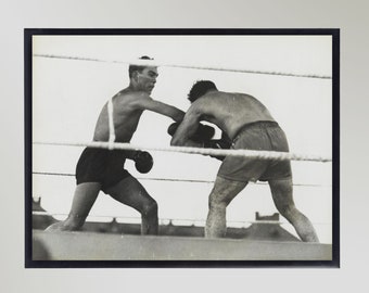 May include: Black and white photograph of two boxers in a boxing ring. The boxer on the left is throwing a punch at the boxer on the right.