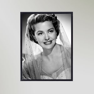 Könnte beinhalten: Schwarzweißes Porträtfoto einer Frau mit einem Schleier über dem Kopf. Sie lächelt und schaut in die Kamera.