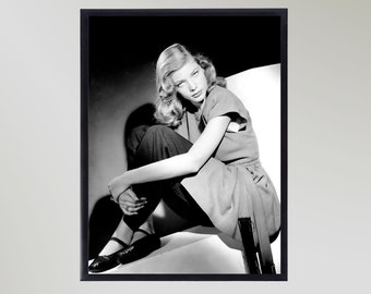 May include: Black and white photo of a woman sitting on a white surface. She is wearing a dark dress and has her hair styled in waves.