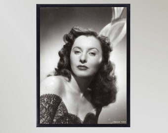 May include: Black and white portrait photograph of a woman with long, wavy hair. She is wearing a low-cut, lace-trimmed dress and looking directly at the camera.