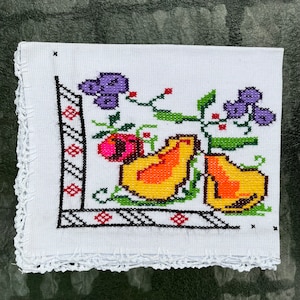 May include: White embroidered kitchen towel with a colorful design of pears, grapes, and leaves. The towel has a crocheted border.