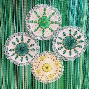 May include: Four white crocheted doilies with green and yellow embroidery. The doilies have a floral design with a central flower and radiating petals.