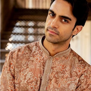 Puede incluir: Una camisa marrón con estampado de flores con cuello mandarín y mangas largas. La camisa tiene un diseño floral con detalles en naranja y blanco.