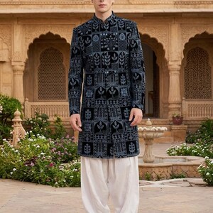 May include: A long-sleeved, dark blue sherwani featuring a repeating grid pattern with intricate light blue floral and botanical embroidery, paired with loose-fitting white trousers and brown leather slip-on shoes with a textured finish.