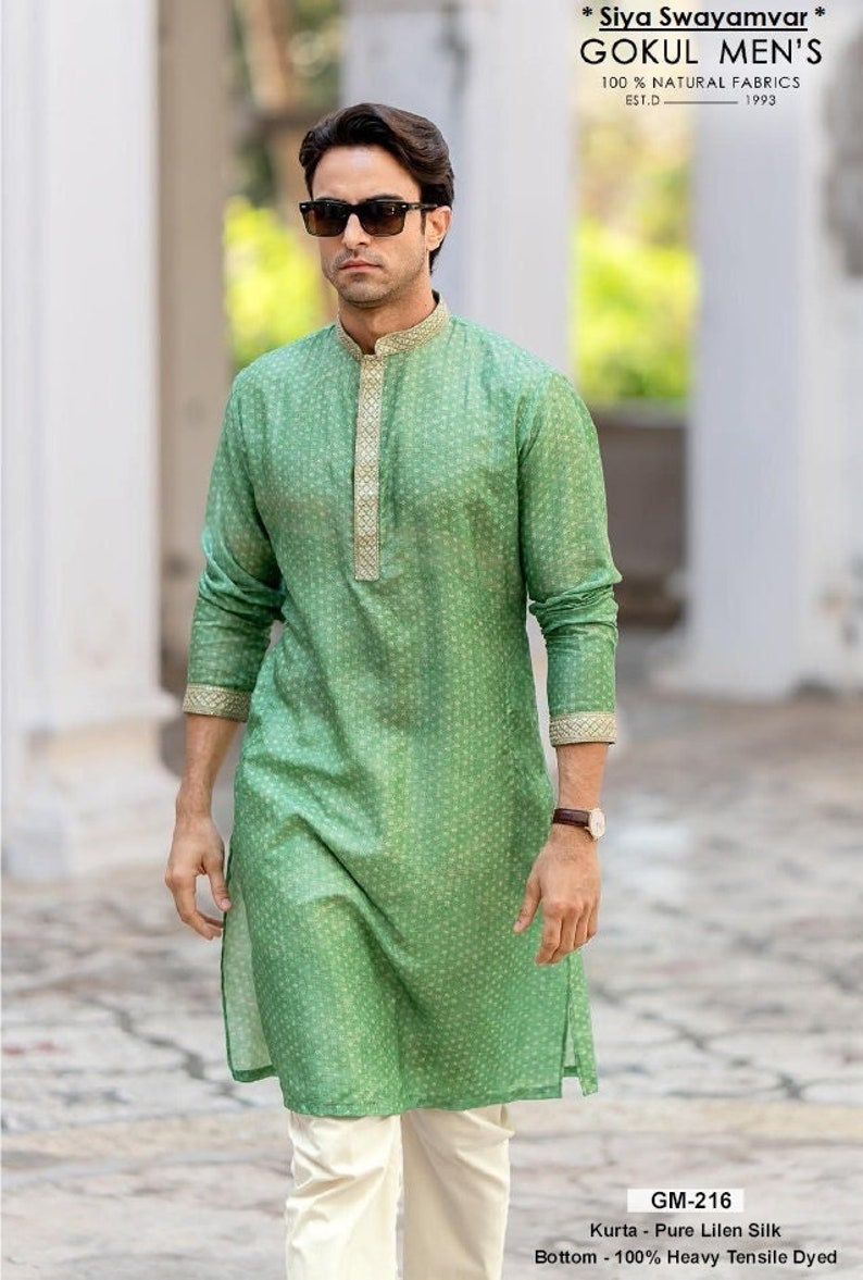 Puede incluir: Un hombre lleva una kurta verde con estampado y ribetes dorados y pantalones blancos. La kurta est&aacute; hecha de pura seda de lino y los pantalones est&aacute;n hechos de tejido te&ntilde;ido resistente pesado. El texto de la imagen dice "* Siya Swayamvar * Gokul Men's 100% Natural Fabrics Est.D 1993 GM-216 Kurta - Pure Lilen Silk Bottom - 100% Heavy Tensile Dyed"