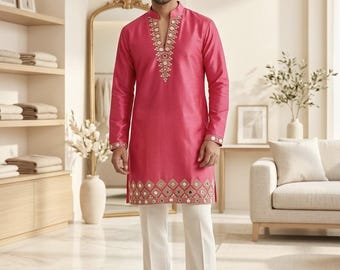 May include: A magenta-colored tunic with intricate embroidery on the neckline and hem, paired with cream-colored trousers. The long-sleeved tunic features a mandarin collar and is worn with brown leather shoes. The outfit is a traditional style.