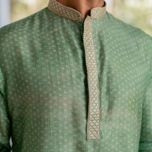 Puede incluir: Una camisa verde con estampado y un ribete bordado blanco y plateado alrededor del cuello y en la parte delantera.