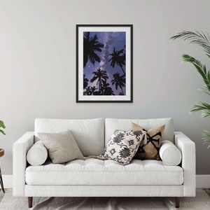 May include: A framed print of a starry night sky with palm trees silhouetted against it. The print is in a black frame and is hanging on a white wall.