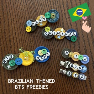 May include: A collection of hair clips decorated with colourful plastic buttons, star-shaped sequins, and white letter beads spelling out ARMY, CRIMINAL, and BTS. The clips feature various shades of blue, green, yellow, and grey, with a Brazilian flag graphic.