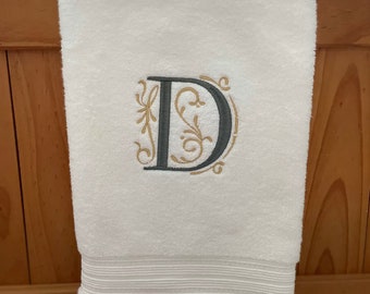 May include: White hand towel with a gray embroidered letter D with gold floral accents.