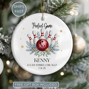 May include: A white ceramic Christmas ornament with a bowling theme. The ornament features a red bowling ball and pins, with the text "Perfect Game" and the name "Kenny". The ornament is decorated with gold stars and greenery.