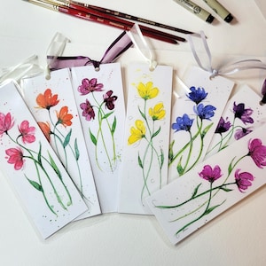 May include: Set of ten watercolor bookmarks featuring different floral designs. Each bookmark is painted with a unique color palette, including pink, purple, yellow, blue, and orange. The bookmarks are tied with a ribbon and are ready to be used.