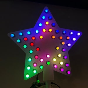 以下が含まれることがあります： 虹色のLEDライトがついた白い星型のクリスマスツリーの飾り。ライトは星の周りに円形に配置されています。
