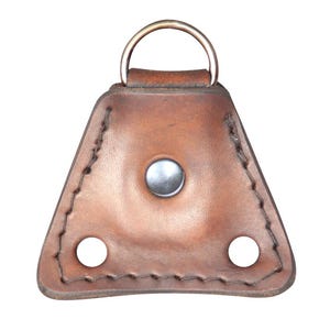 May include: A triangular brown leather accessory featuring a central silver-toned metal snap button, two circular cutouts at the bottom corners, and a silver-toned D-ring attached to the top edge with visible dark stitching along the perimeter.
