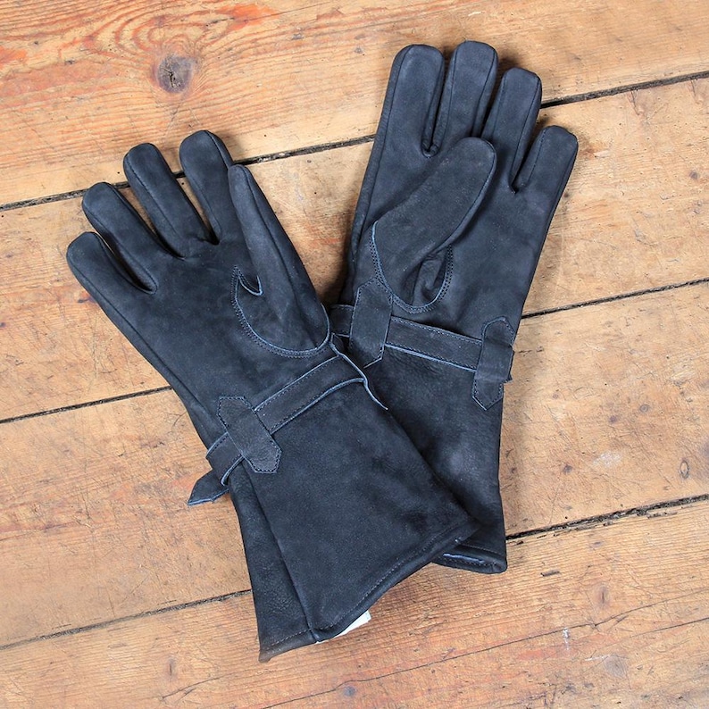 May include: A pair of dark gray leather gloves with long cuffs and buckle details. The gloves are made of a soft, textured leather and are laid out on a wooden surface. The gloves appear to be new and unworn.