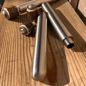 Peut inclure: Un ensemble de tubes cylindriques en métal aux surfaces argentées lisses. Plusieurs tubes sont dotés de bouchons amovibles fabriqués en bois de cerf brun texturé, chacun surmonté d'une petite pièce métallique arrondie.
