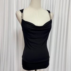 May include: Black cowl neck top with chain straps. The top features a draped neckline and a fitted silhouette. The straps are made of silver-colored chain. The garment is displayed on a mannequin against a white backdrop.