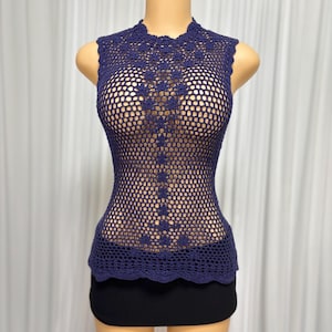 May include: A sleeveless, navy blue crochet top with a high neckline. The top features a delicate floral pattern down the front and a scalloped hem. The open weave design creates a see-through effect.
