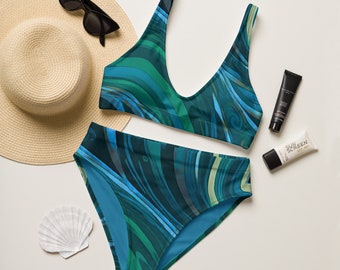 May include: A blue and green patterned bikini with a halter top and high-waisted bottoms. The bikini is laid out on a white surface with a straw hat, sunglasses, and sunscreen.