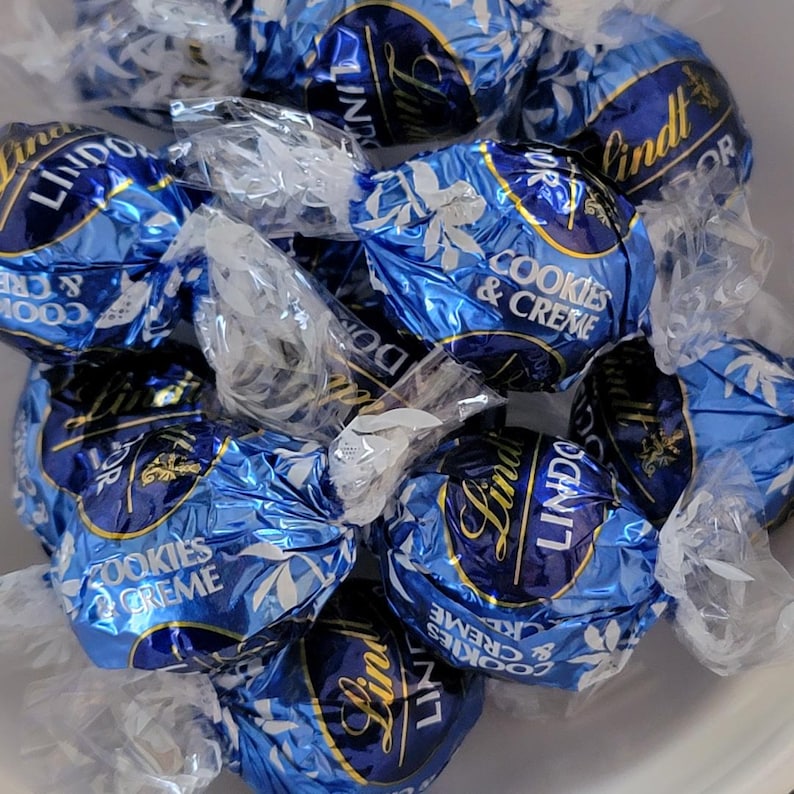 Puede incluir: Un conjunto de trufas de chocolate Lindt Cookies & Creme en envoltorios de papel de aluminio azul y blanco. Los envoltorios presentan el logotipo de Lindt y el nombre del producto. Los caramelos est&aacute;n envueltos individualmente.