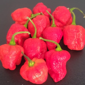 May include: A group of ten red chili peppers, some with green stems, arranged on a black surface. The peppers are all wrinkled and have a bumpy texture.