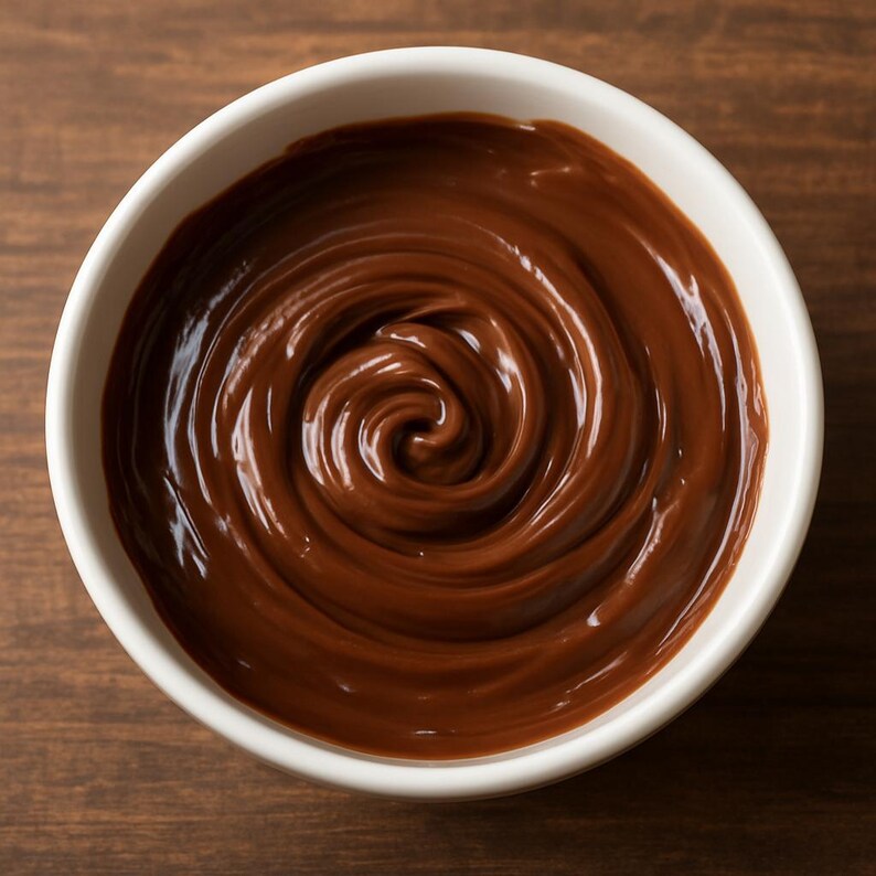 Puede incluir: Un cuenco blanco lleno de salsa de chocolate negro y rica. El chocolate est&aacute; arremolinado en un patr&oacute;n en espiral, creando una apariencia brillante y apetitosa. El cuenco est&aacute; sobre una superficie de madera oscura.