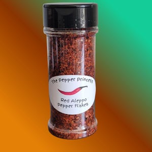 May include: A clear glass jar filled with red Aleppo pepper flakes, topped with a black lid. The jar has a white label with the text "The Pepper Princess" and "Red Aleppo Pepper Flakes" with a red chili pepper illustration.
