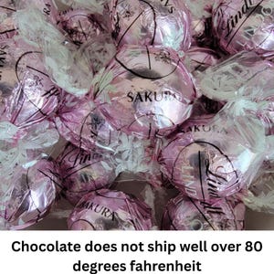 May include: A close-up of a pile of pink and white chocolate truffles wrapped in clear plastic. The truffles are decorated with the word "Sakura" and the brand name "Lindt".