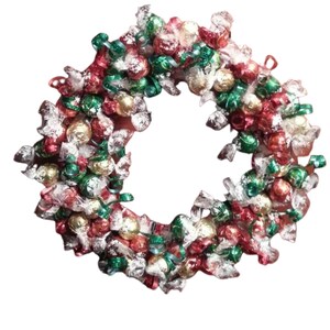 Puede incluir: Una festiva corona navide&ntilde;a hecha de caramelos envueltos en rojo, verde, plateado y dorado. La corona es circular y est&aacute; decorada con cintas, creando una colorida y festiva decoraci&oacute;n navide&ntilde;a.