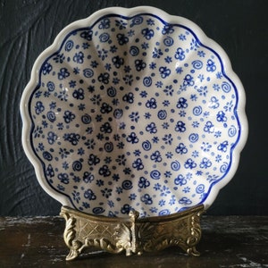 Può includere: Una ciotola in ceramica bianca con un motivo floreale blu e bianco. La ciotola è su un supporto in metallo dorato con tre gambe.