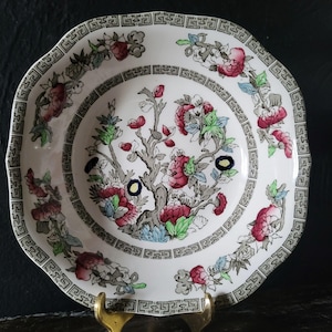 May include: A white ceramic bowl with a green and red floral pattern. The bowl has a square shape with rounded corners and a scalloped edge. The floral pattern features a tree with pink flowers and green leaves.