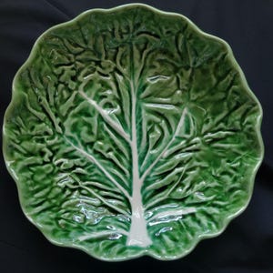 May include: A ceramic bowl shaped like a cabbage leaf with a glossy finish. The bowl features a vibrant green color with a prominent white central vein and smaller branching veins, mimicking the natural texture and appearance of a leafy vegetable.