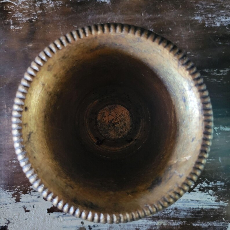 May include: A gold metal vase with a decorative rim. The vase is empty and has a worn, aged look.