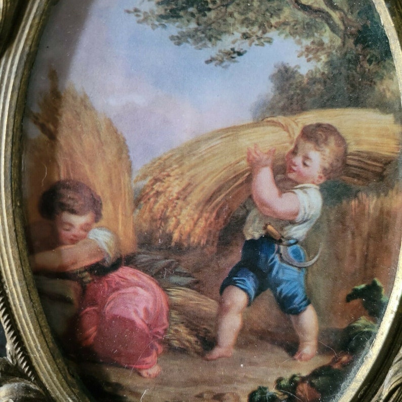 May include: A vintage painting of two children in a field. The child on the left is wearing a pink dress and is looking down. The child on the right is wearing blue pants and a white shirt and is carrying a bundle of wheat on their back. The painting is set against a background of a field of wheat and a blue sky.
