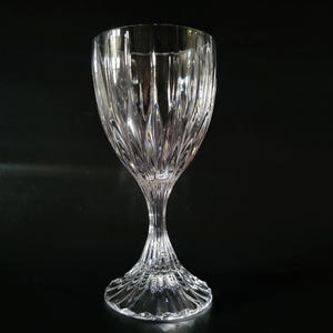May include: A clear crystal wine glass with a textured, vertical pattern. The glass has a long, slender stem and a wide, rounded bowl. The base of the glass is also textured and has a circular design. The glass is set against a black background.