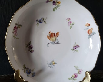 May include: White porcelain plate with a scalloped edge and gold trim. The plate is decorated with hand-painted floral designs in shades of orange, pink, purple, and blue. The plate is displayed on a gold-colored stand.