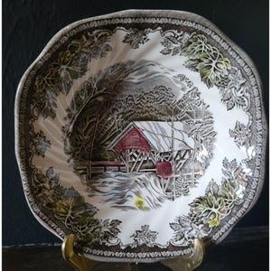Peut inclure: Un bol en céramique blanche avec un motif floral brun et vert. Le bol représente une scène de pont couvert dans un paysage enneigé.