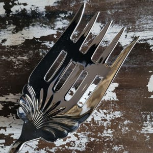 May include: A polished silver serving fork with a decorative floral handle. The fork features multiple tines and slots, reflecting light. This utensil is designed for serving food, suitable for formal dining occasions or events.