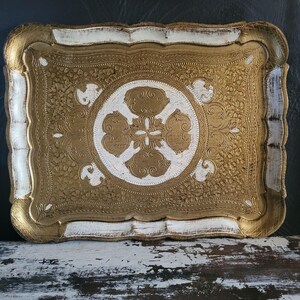 May include: Rectangular decorative tray with a gold and white ornate design. The tray features a gold floral pattern on the interior, with a white border and accents. The tray's edges are scalloped, and the overall aesthetic is vintage.