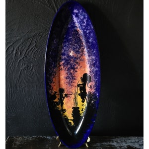 Könnte beinhalten: Eine ovale Servierplatte aus Keramik mit blauer Glasur und einem handgemalten Motiv von zwei Silhouetten vor einem Sonnenuntergang. Die Figuren stehen in einem Wald mit Bäumen und einem Stern am Himmel.