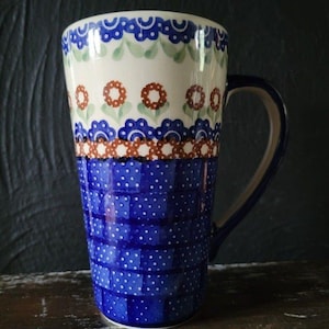 May include: A tall, blue and white ceramic mug with a floral design and a polka dot pattern. The mug has a handle and is perfect for enjoying a hot beverage.