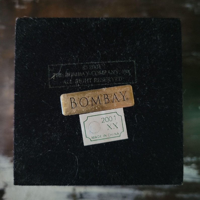 May include: A black velvet box with a gold label that reads "BOMBAY" and a smaller green label that reads "2001 XX MADE IN CHINA".