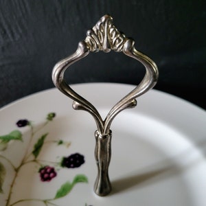 May include: A silver serving stand with a decorative handle and a white plate with a blackberry design.