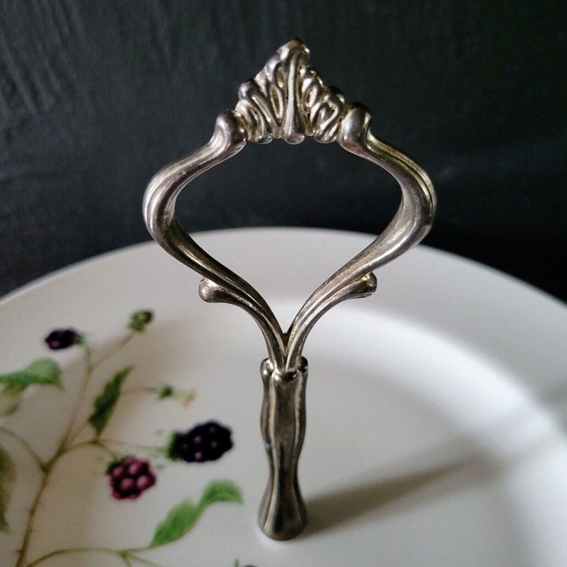 May include: A silver serving stand with a decorative handle and a white plate with a blackberry design.