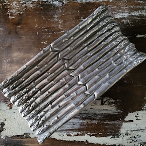 May include: Silver asparagus serving dish with a textured design. The dish is shaped like a bundle of asparagus.
