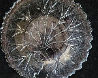Puede incluir: Un plato de vidrio transparente con un diseño en relieve de una hoja. El plato tiene un borde festoneado.