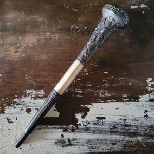 May include: A silver walking stick with an ornate handle and a white, ivory-like shaft. The stick is lying on a wooden surface.