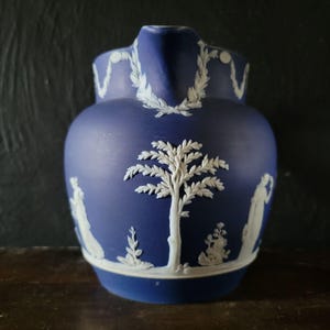 May include: A blue and white ceramic pitcher with a tree and figures in relief. The pitcher is decorated with a white floral design.