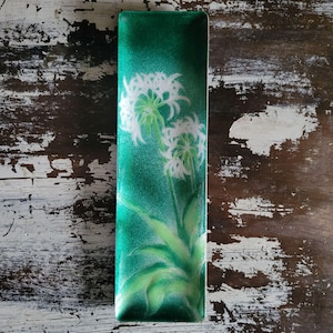 Op de afbeelding: Rechthoekige, smaragdgroene decoratieve schaal met een bloemenontwerp. De schaal heeft een handgeschilderde afbeelding van witte bloemen met groene stelen en bladeren. De achtergrond heeft een glinsterend, gestructureerd uiterlijk. De schaal is waarschijnlijk gemaakt van glas of keramiek.